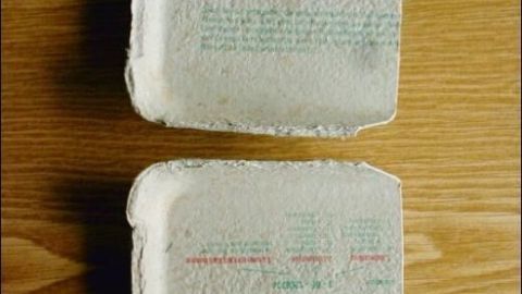 Kartonschalen liegen geöffnet auf Holztisch, beschriftet mit "Frische Eier mit". Sie wirken gebraucht und schlicht.