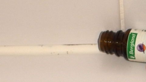 Ein Fläschchen Teebaumöl steht schräg auf einer weißen Oberfläche, bereit zur Anwendung gegen Schimmel und Pilze.