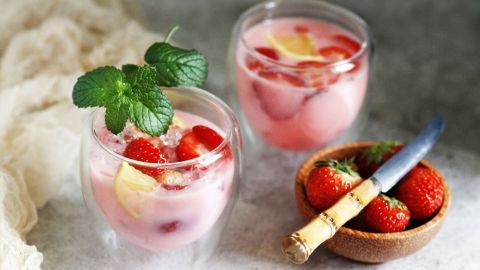 Zwei Gläser mit alkoholischer Erdbeerbowle stehen auf einer hellen Oberfläche, umgeben von frischen Erdbeeren und einem Messer.