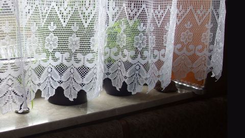 Transparente, knitterfreie Gardinen hängen am Fenster und lassen sanftes Licht auf die Fensterbank mit Blumen scheinen.