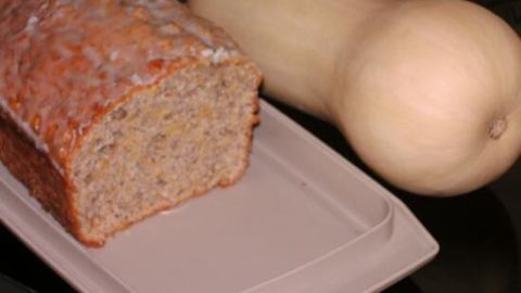 Ein frisch gebackener Kürbiskuchen steht auf einem Teller neben einem ganzen Kürbis, umgeben von einer dunklen Oberfläche.