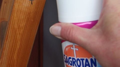 Mit Desinfektionsmittel wasserfesten Stift auf Möbeln entfernen. Ein Hand hält eine Flasche Desinfektionsmittel, während es auf einem Holzmöbelstück mit einem wasserfesten Stift arbeitet.