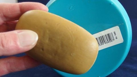 Eine Hand hält einen Seifenstück, während es sich über einen blauen Behälter mit einem Aufkleber befindet.