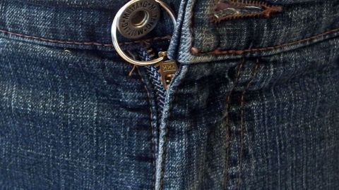 Ein Reißverschluss an einer Jeans öffnet sich, während der Stoff blau und eng anliegend ist. Die Metallteile glänzen.