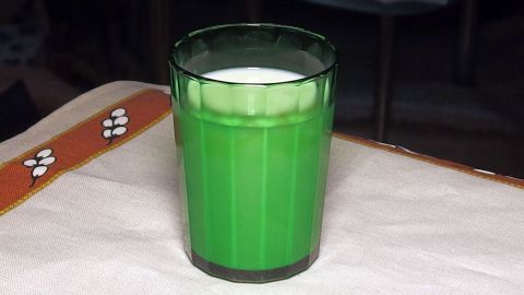 Ein grüner Drink in einem hohen Glas steht auf einem Tisch, umgeben von einem neutralen Hintergrund. Der Geruch in der Wohnung könnte durch diese Flüssigkeit entstehen.