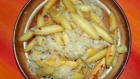 Auf einem bunten Teller liegen goldene Schupfnudeln, die mit frischem, weißem Sauerkraut umgeben sind.