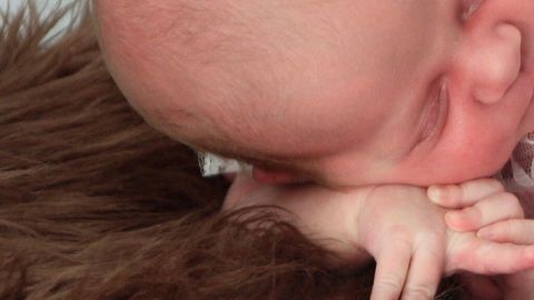 Ein schlafendes Baby mit Milchschorf liegt sanft auf einem braunen, fellähnlichen Stoff. Die Umgebung wirkt beruhigend.