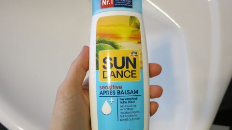 Eine Flasche Après-Balsam wird von einer Hand gehalten. Der Balsam dient zur Hautpflege nach der Intimrasur.