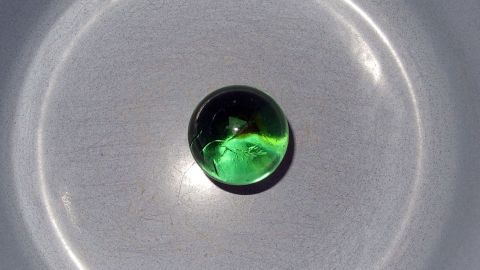 Das Anbrennen von Speisen vermeidet man mithilfe einer Glaskugel. Eine grüne Kugel auf einer glatten Oberfläche reflektiert Licht und zeigt so die Wichtigkeit, Anbrennen zu vermeiden.