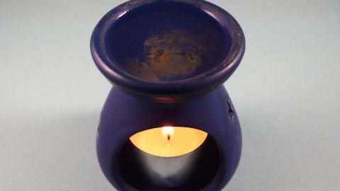 Ein lila Duftöl-Gefäß steht auf einer glatten Oberfläche, während eine Kerze im Inneren brennt und Aroma verbreitet.