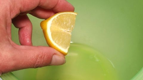 Eine Hand hält ein Zitronenstück über eine grüne Schüssel, bereit, den Saft in das steife Eiweiß zu pressen.