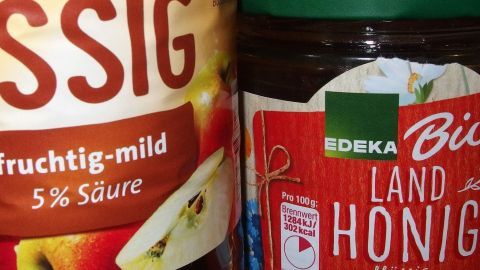 Eine Flasche Essig und ein Glas Honig stehen nebeneinander auf einer Oberfläche, bereit zur Verwendung in Omas Rezept bei Magen-Darm-Grippe.