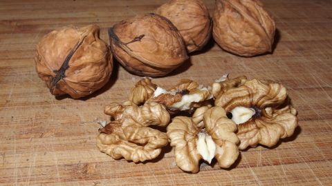 Mit zerkleinerten Walnüssen kann man Frikadellen verfeinern. Einfach in den Hackfleischteig hinzugeben. Walnüsse liegen auf einem Holzbrett, während geschälte Stücke daneben liegen, bereit zum Verfeinern von Frikadellen.