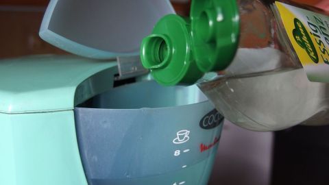 Eine Hand gießt Essig in eine Kaffeemaschine, um den Kunststoffgeschmack zu beseitigen und den Kaffee zu verbessern.