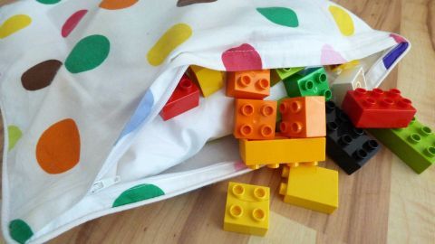 Bunte Duplo-Steine fallen aus einer gepunkteten Tasche auf einen Holzfußboden und warten darauf, gereinigt zu werden.