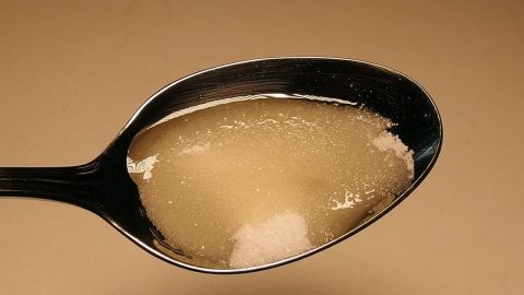Ein Löffel mit einem süßlichen Sirup und Zucker liegt vor einem hellen Hintergrund, um Linderung bei starkem Husten in der Nacht zu bieten.
