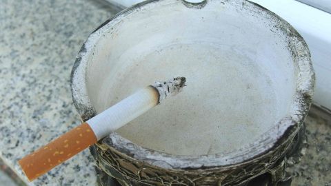 Mit Rasierschaum Rauchgeruch von den Händen entfernen. Ein Zigarettenstummel steckt in einem rustikalen Aschenbecher, der auf einer grauen Oberfläche steht, um Rauchergeruch zu vermeiden.