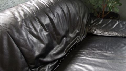Ein schwarzes Ledersofa ruht in einer eleganten Umgebung, die Polsterung ist leicht zerknittert und glänzend.