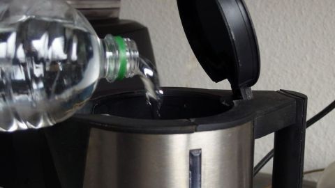 Eine Wasserflasche schüttet Flüssigkeit in einen Entkalker, während dieser auf einer Küchentheke steht.