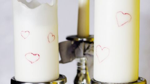 Drei Kerzen auf silbernen Haltern, eine davon tropft, während sie in einer ruhigen, hellen Umgebung stehen und Herzen zeigen.