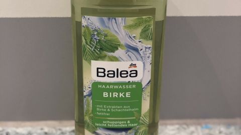 Ein grün beschrifteter Flasche mit Birkenwasser steht auf einem bunten, steinigen Untergrund und könnte gegen Schuppen helfen.