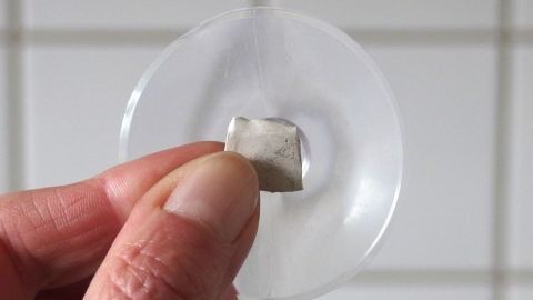 Saugnäpfe auf rauhen Fliesen anbringen - mit "Kaugummikleber". Ein Saugnapf wird mit Kaugummikleber an einer rauen Fliese befestigt, während im Hintergrund weiße Fliesen sichtbar sind.