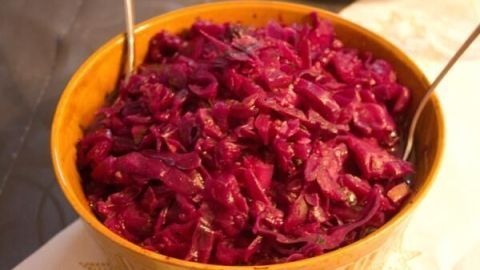 Rotkohl in einer gelben Schüssel, servierbereit mit Besteck, steht auf einem Tisch mit einer weißen Tischdecke und Sternchenmuster.