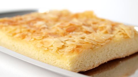 Ein Butterkuchen liegt auf einem silbernen Blech, mit einer goldbraunen Oberfläche und dekorativen Mandelscheiben darauf.