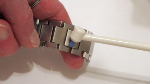 Eine Hand hält eine Munddusche, die mit Wasserdruck eine Uhrmitte reinigt, auf einem weißen Tisch.