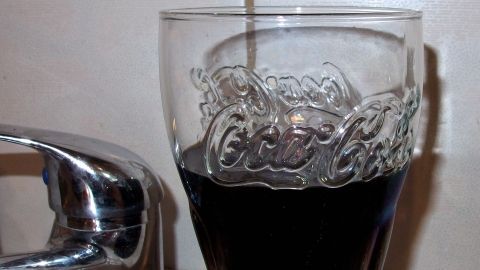 Ein Glas Cola steht neben einem Wasserhahn, während Cola langsam hineingegossen wird, um den Abfluss zu reinigen.