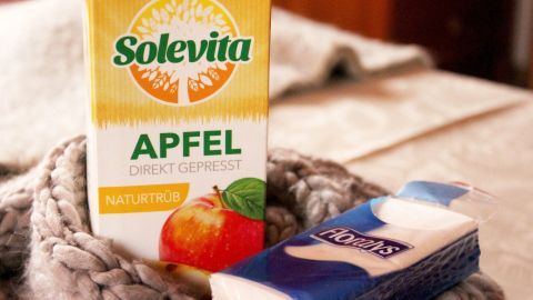 Durch das Erhitzen des Apfelsaftes werden ätherische Öle frei, die Erkältungsbeschwerden wie Halsschmerzen lindern. Eine Packung naturtrüber Apfelsaft steht auf einer chemischen Decke, während sie in einem warmen Raum auf einem Tisch liegt.