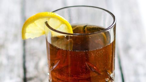 Ein Glas mit einer dunklen, eisgekühlten Flüssigkeit steht auf rustikalem Holz, garniert mit einer Zitronenscheibe.