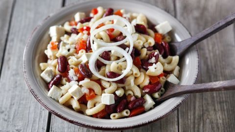 Ein bunter Nudelsalat mit Schafskäse und Bohnen, angerichtet in einer Schüssel und umgeben von Holzoberfläche.