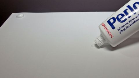 Eine Zahnpastatube steht über einem weißen Poster, bereit, um Spuren zu hinterlassen und es zu befestigen.