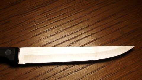 Ein scharfes Messer liegt still auf einer hölzernen, leicht strukturierten Tischoberfläche, kontrastreich beleuchtet.