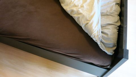 Ein Bett mit einer braunen Matratze und einer weißen Decke, die unordentlich am Rand liegt, sorgt für kalte Füße im Bett.