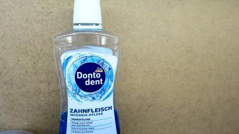 Flasche Donodent Zahnfleisch Intensiv-Pflege Mundspülung steht auf Holzregal. Text: Ohne Alkohol, schützt vor Karies.