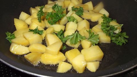 In einer Pfanne braten Würfelkartoffeln mit frischer Petersilie, um das Gericht Honig-Petersilien-Kartoffeln zuzubereiten.