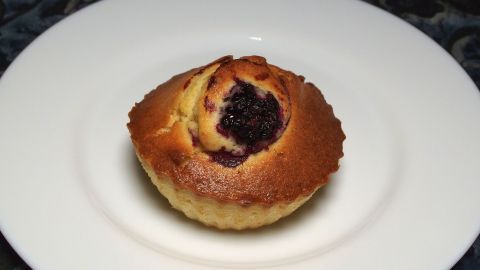 Ein Muffin steht auf einem weißen Teller, frisch gebacken und leicht goldbraun, mit einer dunklen Füllung oben.