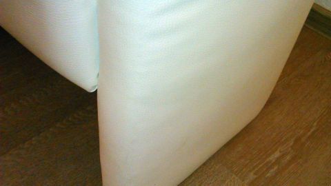 Eine weiße Ledercouch steht auf einem Holzboden, sichtbar ist die Ecke des Sofas, das vermutlich gereinigt wird.