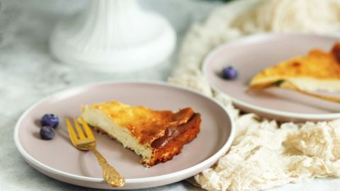 Ein Käsekuchen ohne Boden steht auf einer eleganten Tortenplatte, mit einem Stück auf einem Teller und Blaubeeren daneben.