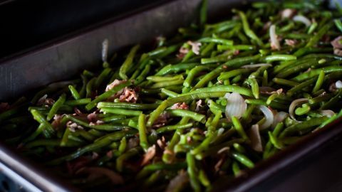 Grüne Bohnen in einer Schale, gemischt mit Zwiebeln und etwas Fleisch, bereit zum Servieren in einer Essensumgebung.