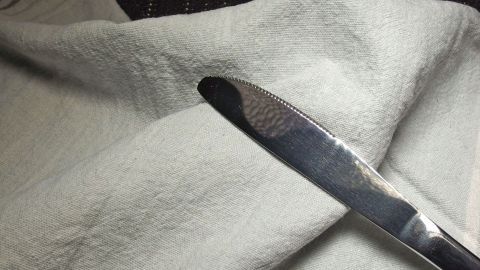 Ein Messer liegt auf einem blassen Tuch, das zur Entfernung von Blutflecken genutzt wird, vermutlich in einem gemütlichen Raum.