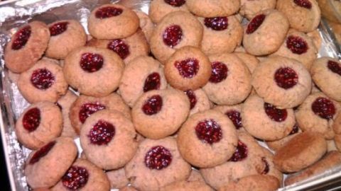 Plätzchen mit Himbeermarmelade in der Mitte liegen dicht an dicht in einer silbernen Backform.