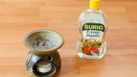 Eine Duftlampe steht neben einer Flasche Essig auf einem Holzuntergrund, bereit zum Reinigen mit Essig.