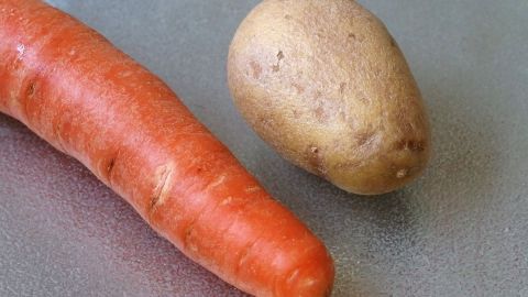 Eine Karotte und eine Kartoffel liegen nebeneinander auf einer glatten Oberfläche und symbolisieren natürliche Lebensmittel gegen Durchfall.