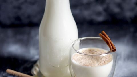 Ein Glas mit Milch, Zimtstangen verziert, steht neben einer Flasche Milch auf einem silbernen Tablett.
