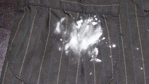 Ein Kleidungsstück mit einem großen Mehlflecken auf der Tasche liegt auf einem dunklen Untergrund.