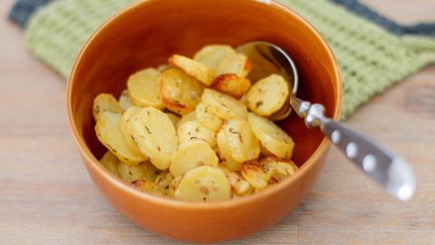 Knusprige Ofenkartoffeln liegen in einer rustikalen Schüssel, daneben ein Löffel, auf einem grün-weißen Topflappen.