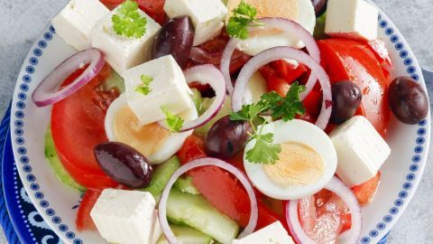 Ein bunter griechischer Bauernsalat mit Ei, Feta, Oliven und frischem Gemüse auf einem schönen Teller.